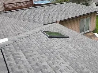 An elevated view of a gray asphalt shingle roof featuring a rectangular skylight and an attached wooden deck.