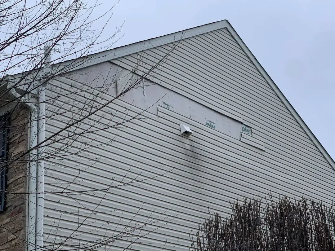Exterior view of a gable wall with light-colored horizontal siding and a security camera mounted near a rectangular vent.