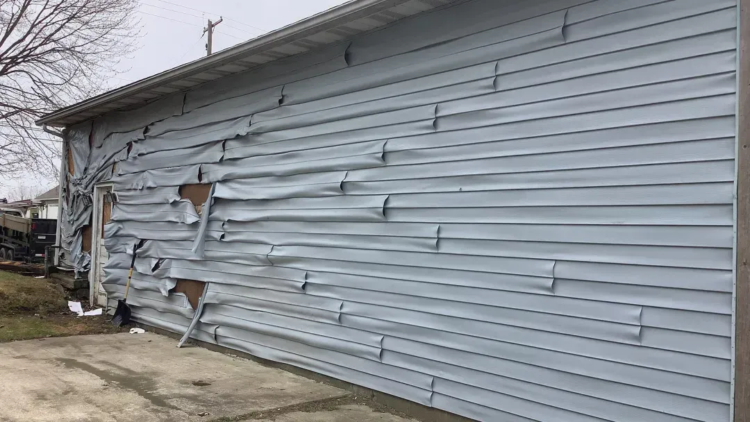 A side view of a building with light gray vinyl siding that has melted and warped from heat damage.