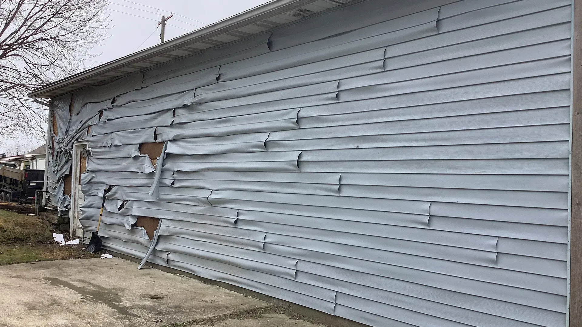 Light blue vinyl siding is severely warped and damaged on the exterior wall of a building.