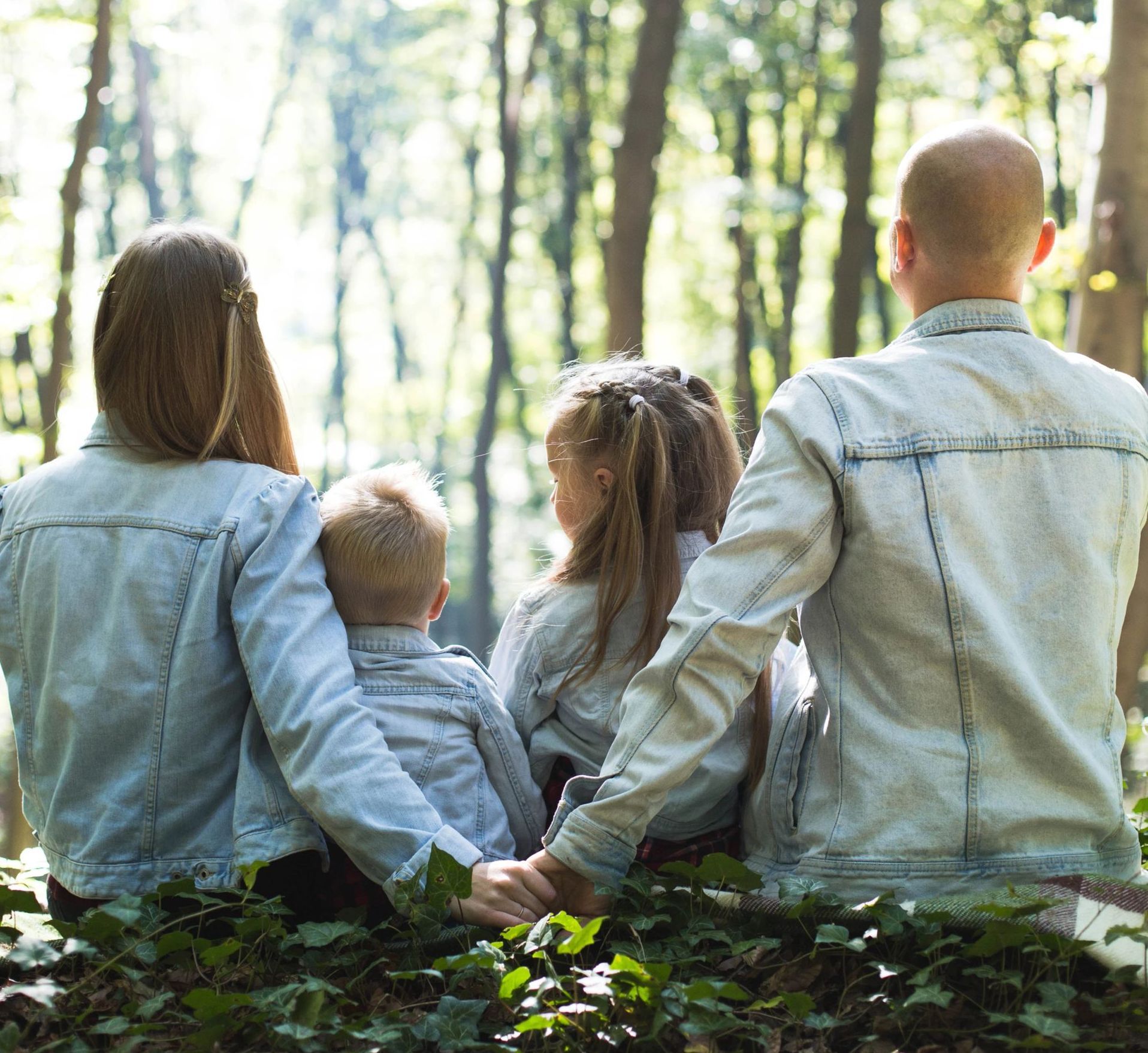 A family is sitting on the ground in the woods holding hands.