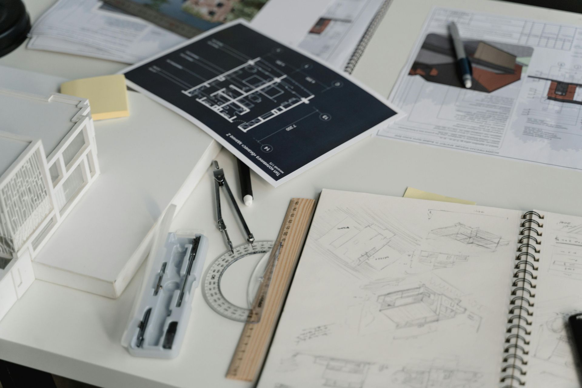 Architectural drafting workspace with blueprint, notebook sketches, ruler, compass, and model