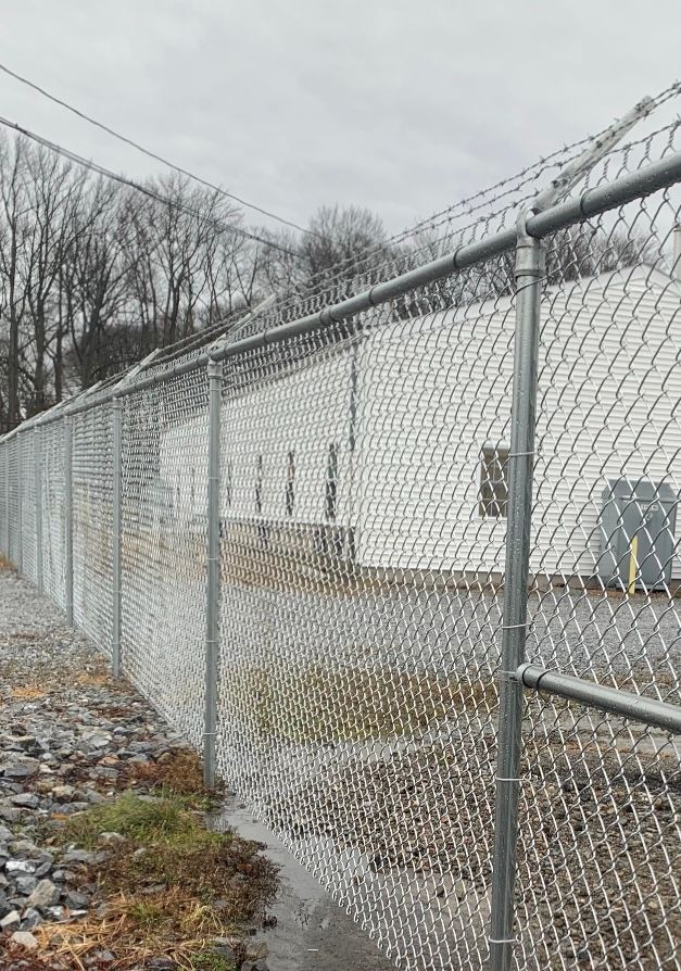 Chain-link fence along a wet roadside beside a white industrial building on an overcast day