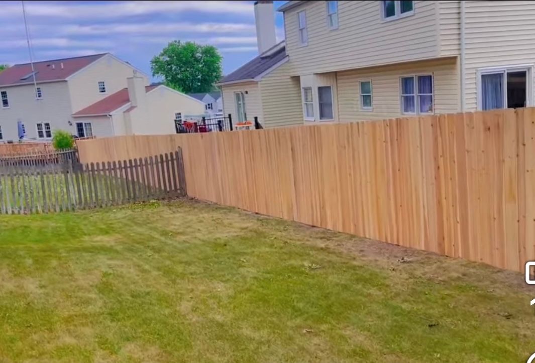 Backyard with green lawn, wooden fence, and beige suburban houses under a cloudy sky