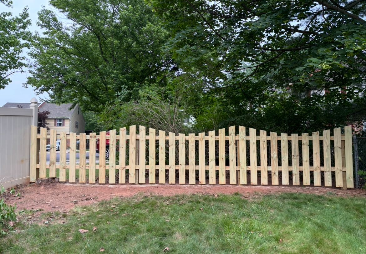 Wooden picket fence in a backyard with trees and grass