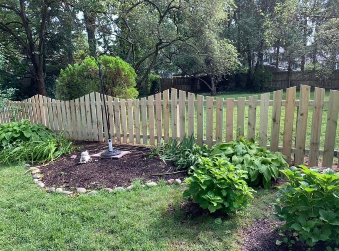 Wooden picket fence bordering a lush garden with green plants and trees