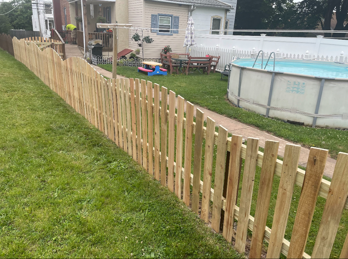 Wooden fence along a grassy yard beside a house and above-ground pool