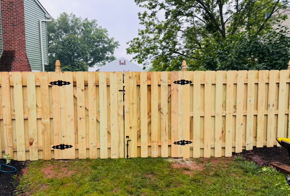 New wooden fence with black hinges in a backyard, bordered by grass and trees