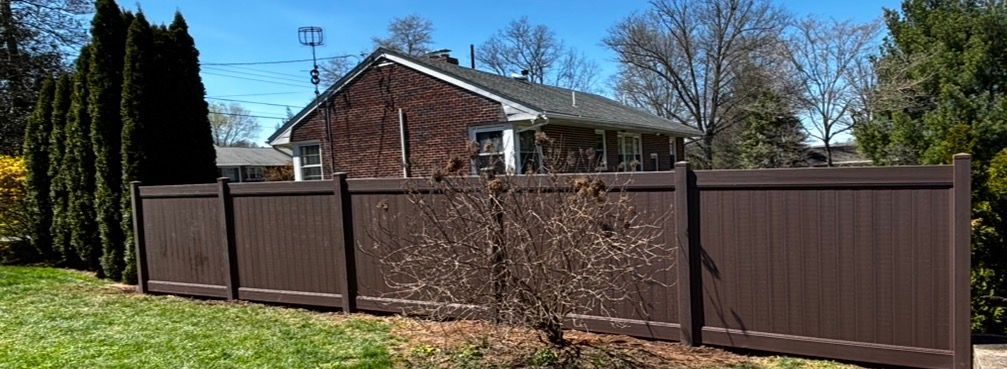 Brown wooden fence in front of a brick house on a sunny suburban street
