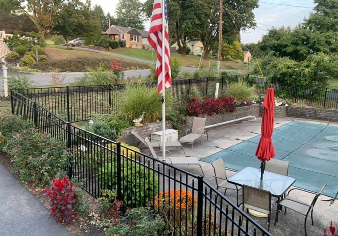 Backyard pool and patio with American flag, black fence, lounge chairs, and red umbrellas