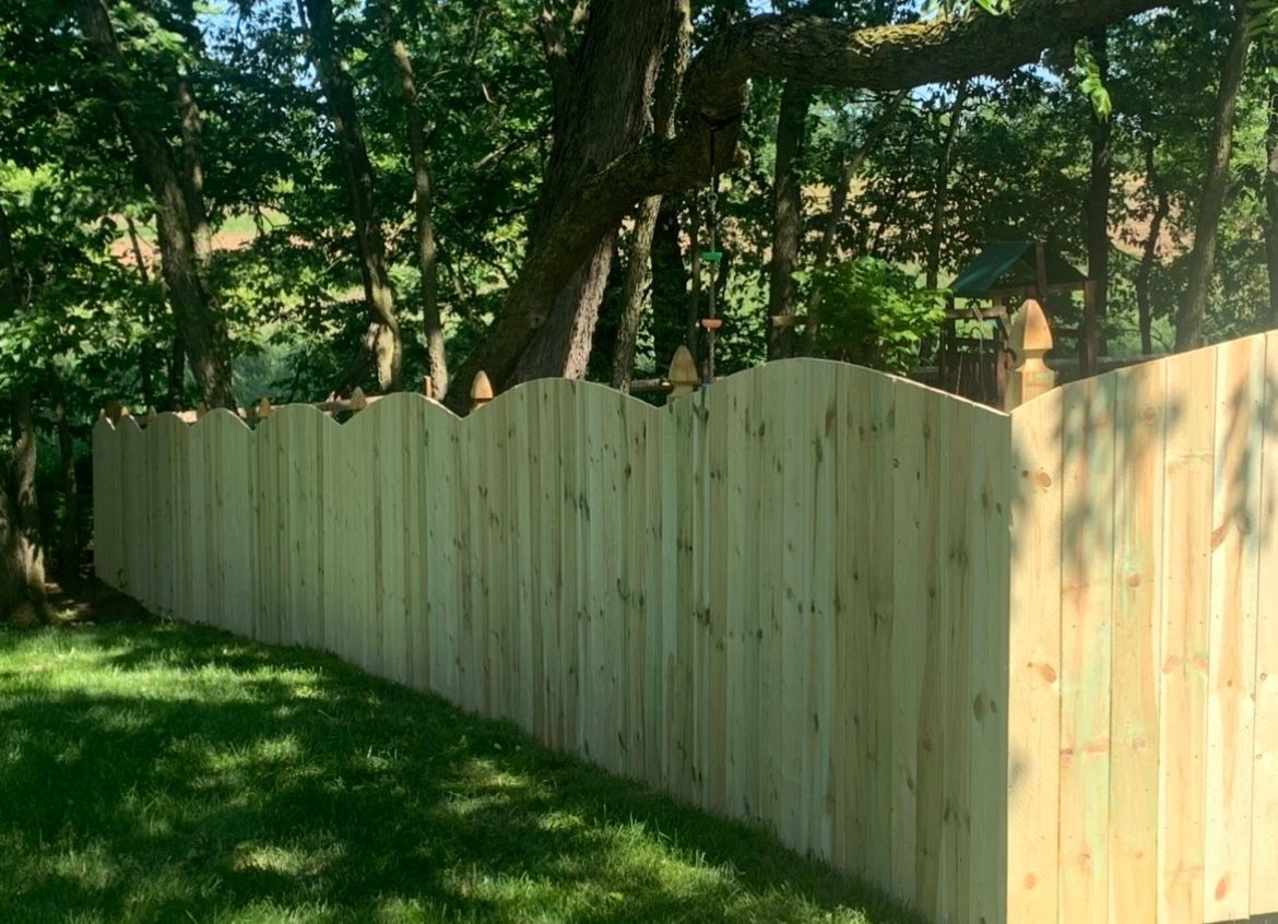 Light wooden fence along a grassy yard beside trees in dappled sunlight