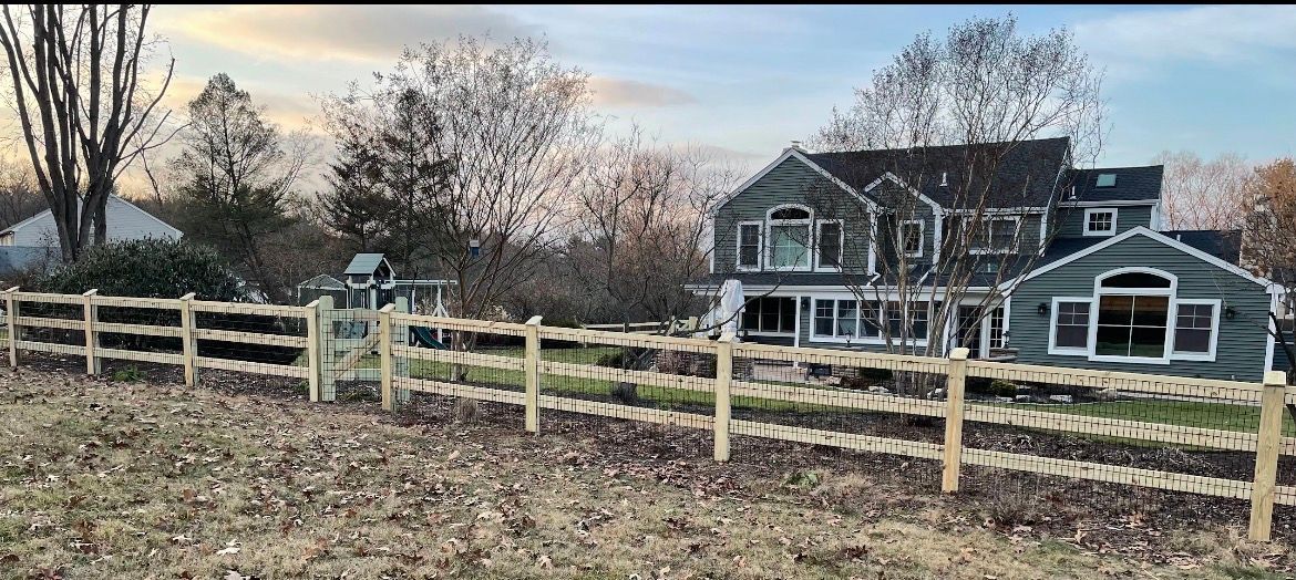 A farmhouse with a porch and fenced yard in a leaf-strewn rural setting at dusk.