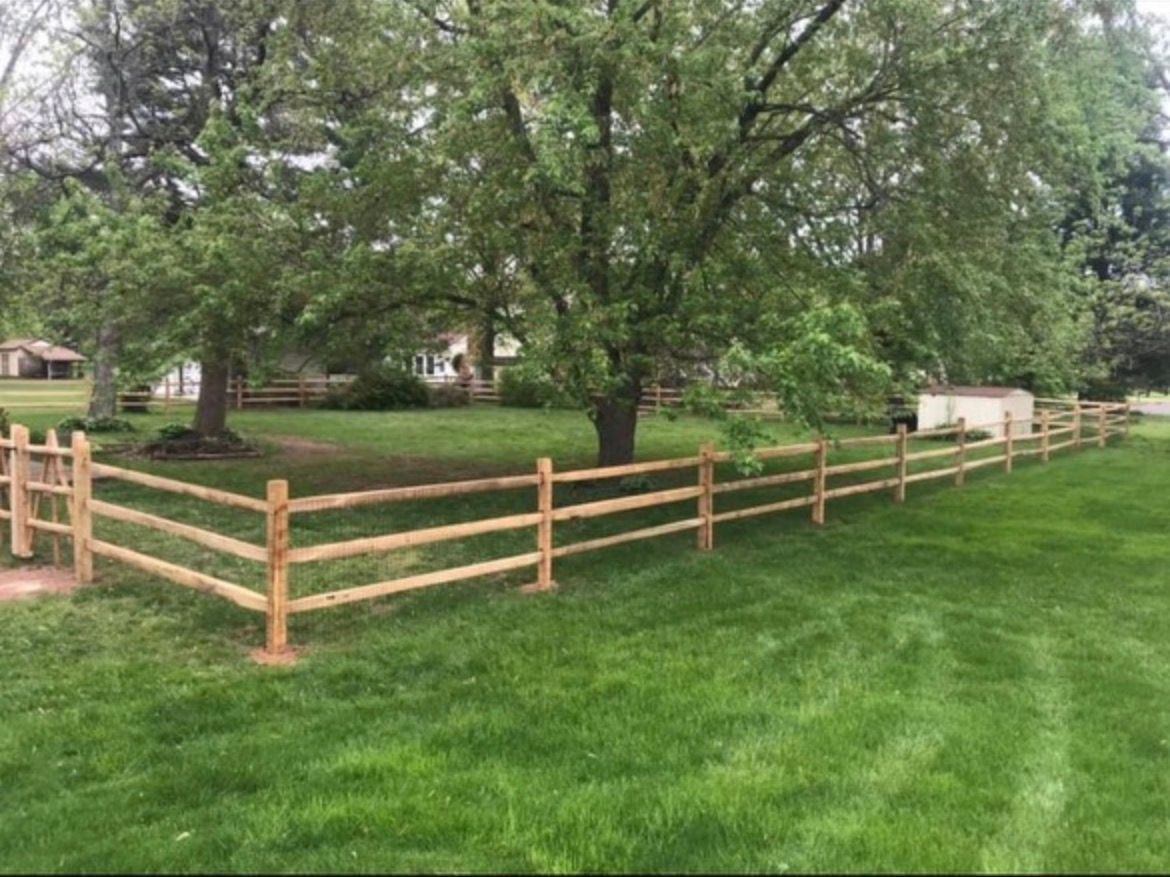 Wooden fence enclosing a lush green yard with large trees and houses in the background