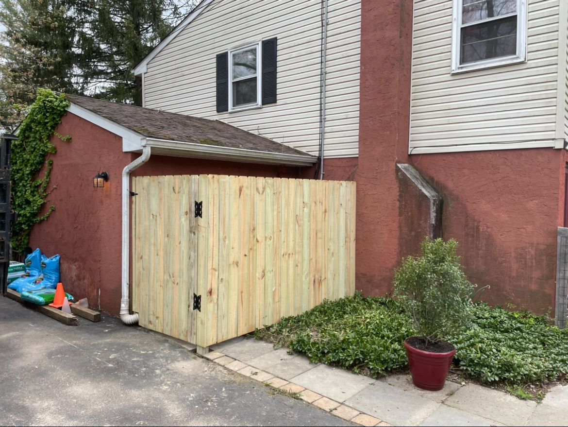 Wooden shed beside brick house with a small paved area and potted plant