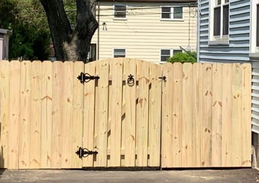 Light wood double gate with black hinges and latch in a fenced residential yard