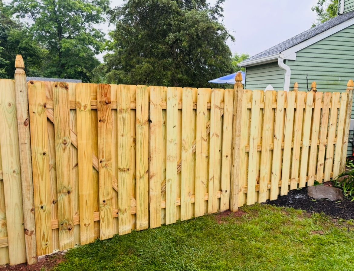 New wooden fence along a grassy yard beside a green house