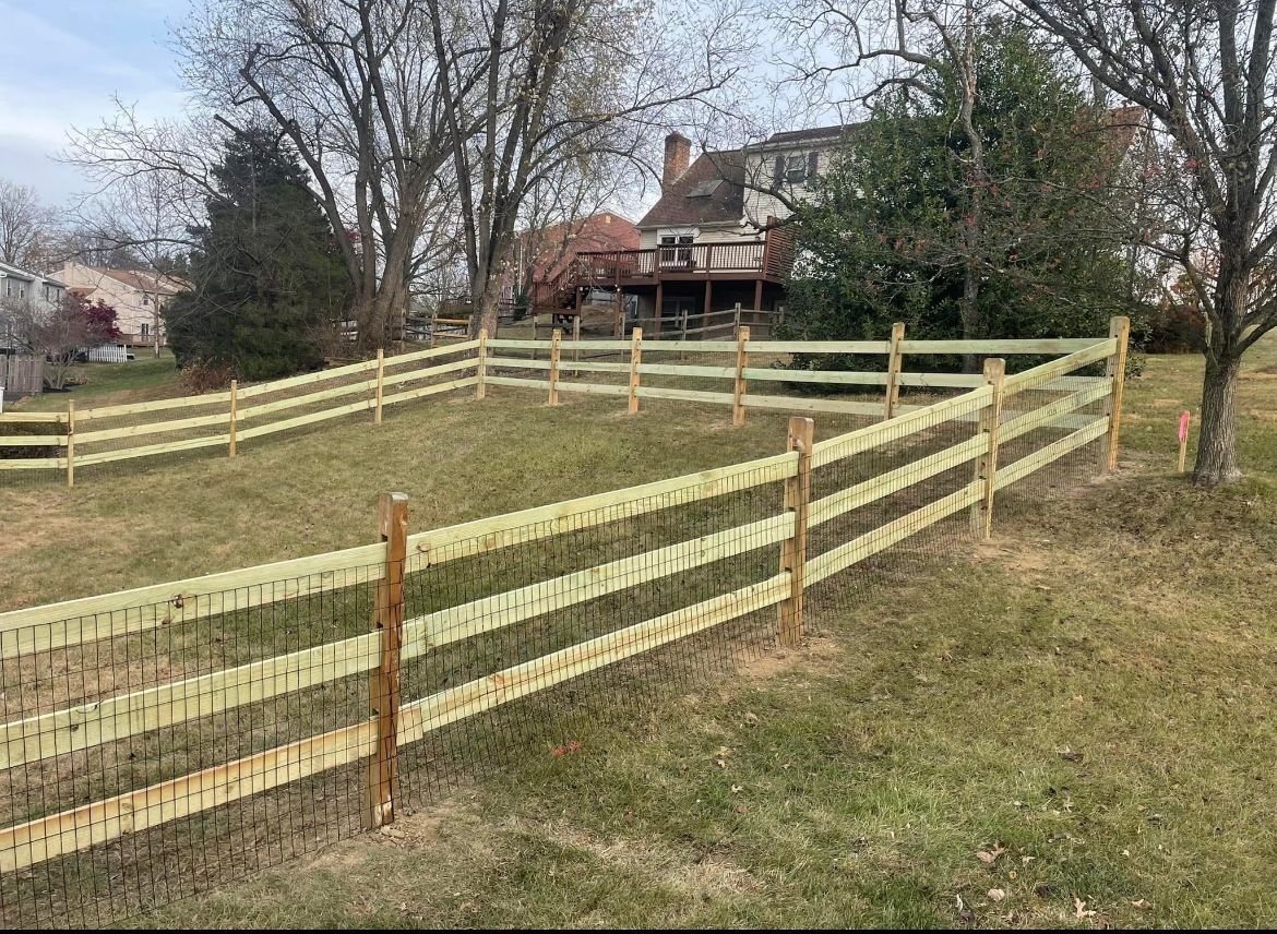 Wooden fence lining a grassy hillside with a house and trees in the background