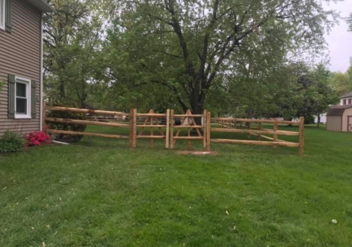 Wooden fence in a grassy backyard with trees and a house at left under a cloudy sky