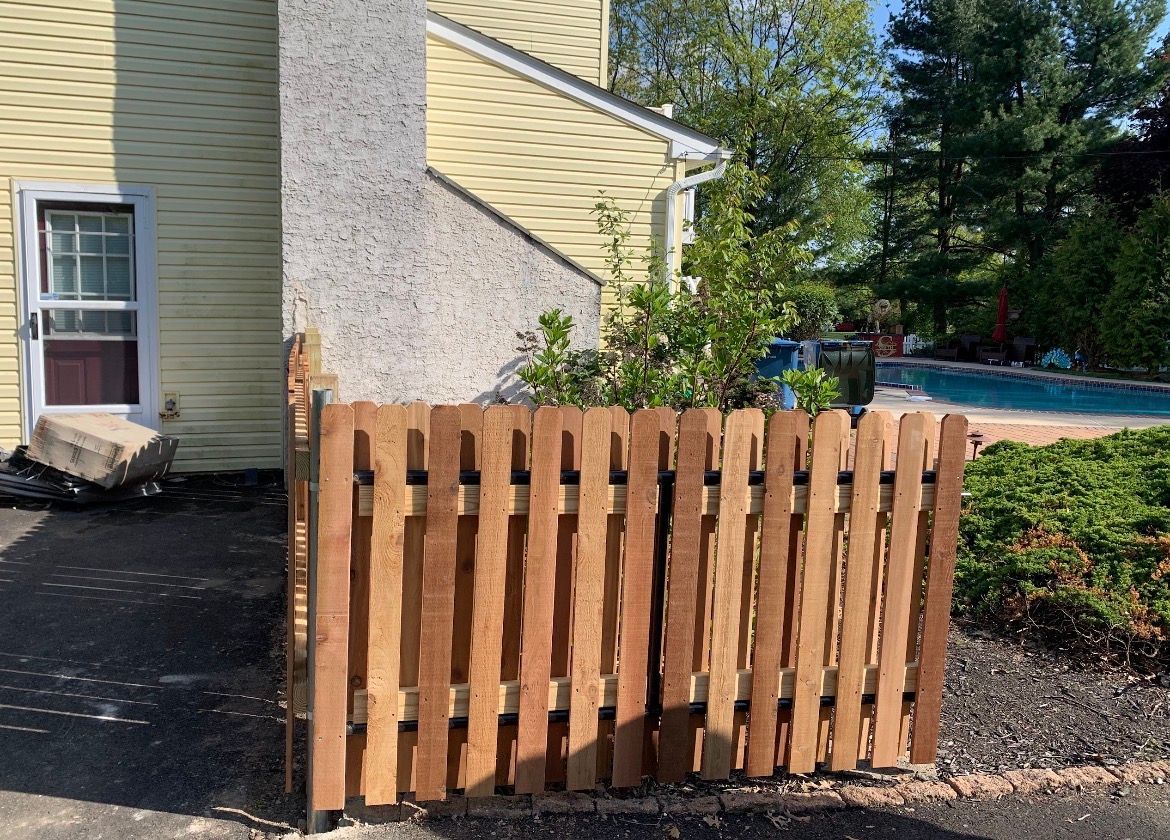 Wooden pallet gate in front of a house, beside a driveway and pool area.