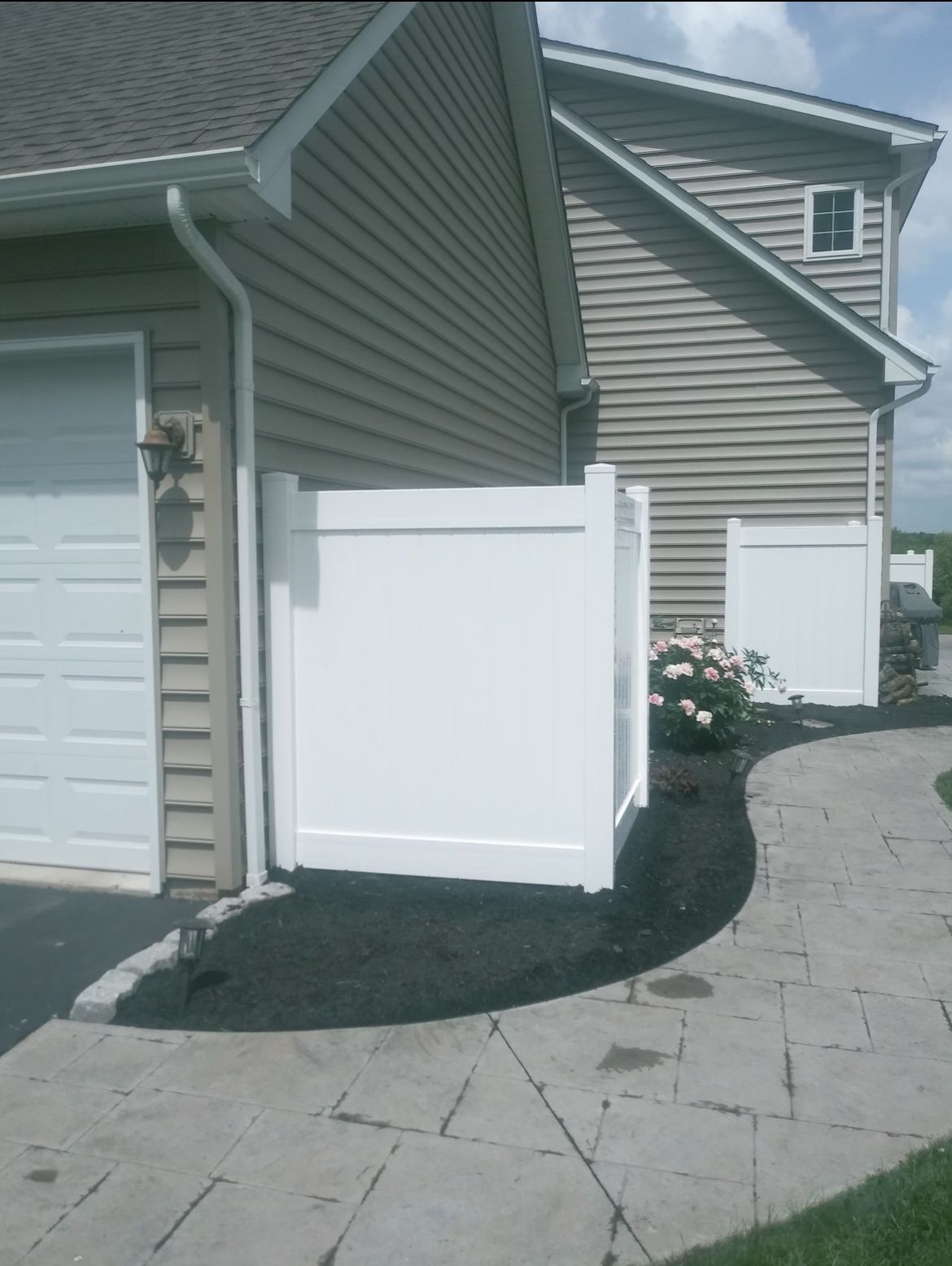 White vinyl fence panels beside beige townhouse garages along a curved stone driveway.