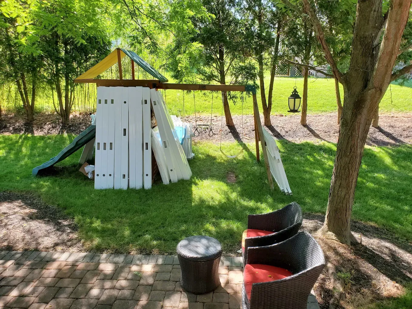 Backyard play fort with slide and red tunnel, surrounded by trees and grass in shade