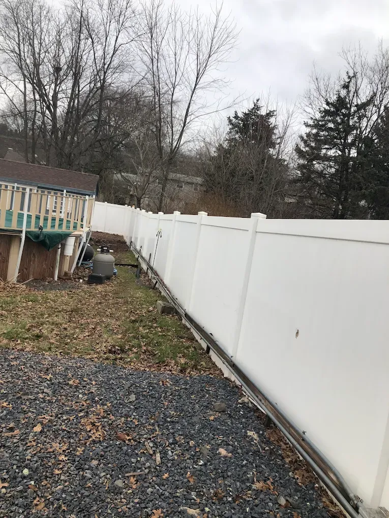 Backyard with white vinyl fence, gravel path, small deck, and leafless trees under a gray sky