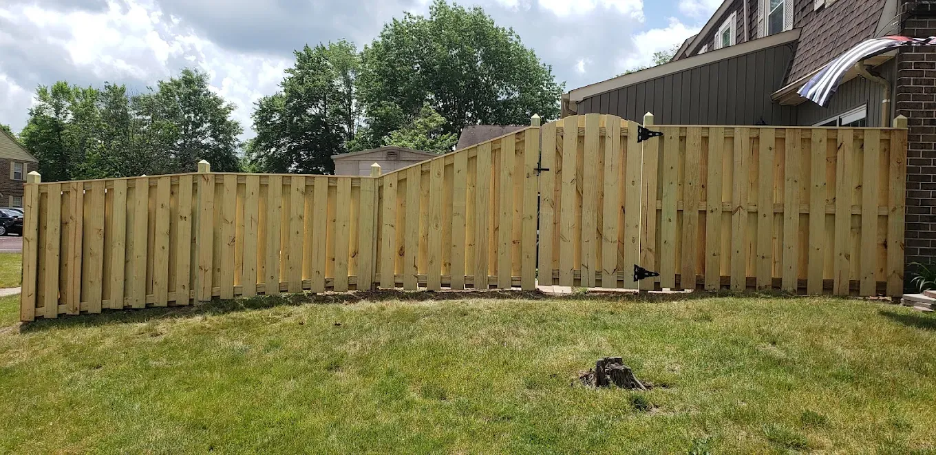 Wooden privacy fence with a wavy top along a grassy yard under cloudy skies