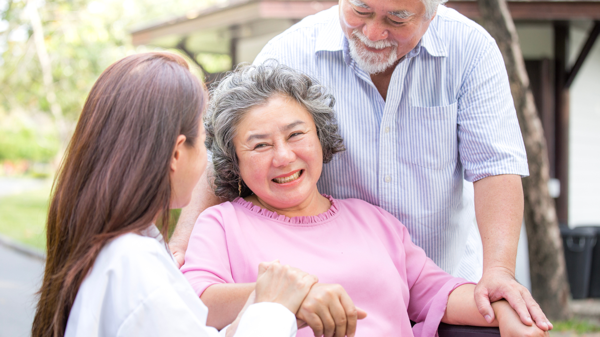A woman is holding the hand of an elderly woman while a man and woman look on.