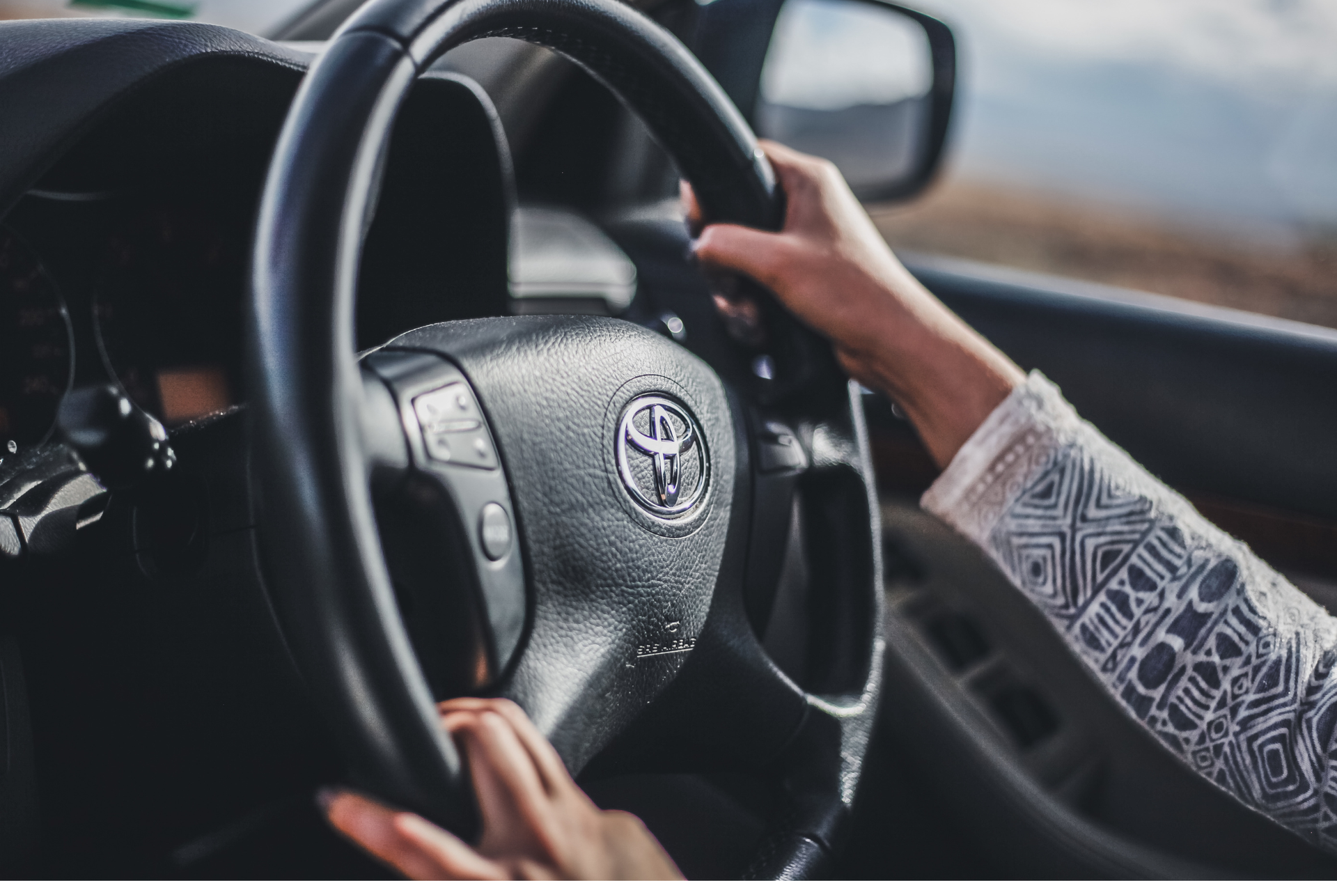 A person is holding the steering wheel of a toyota car.