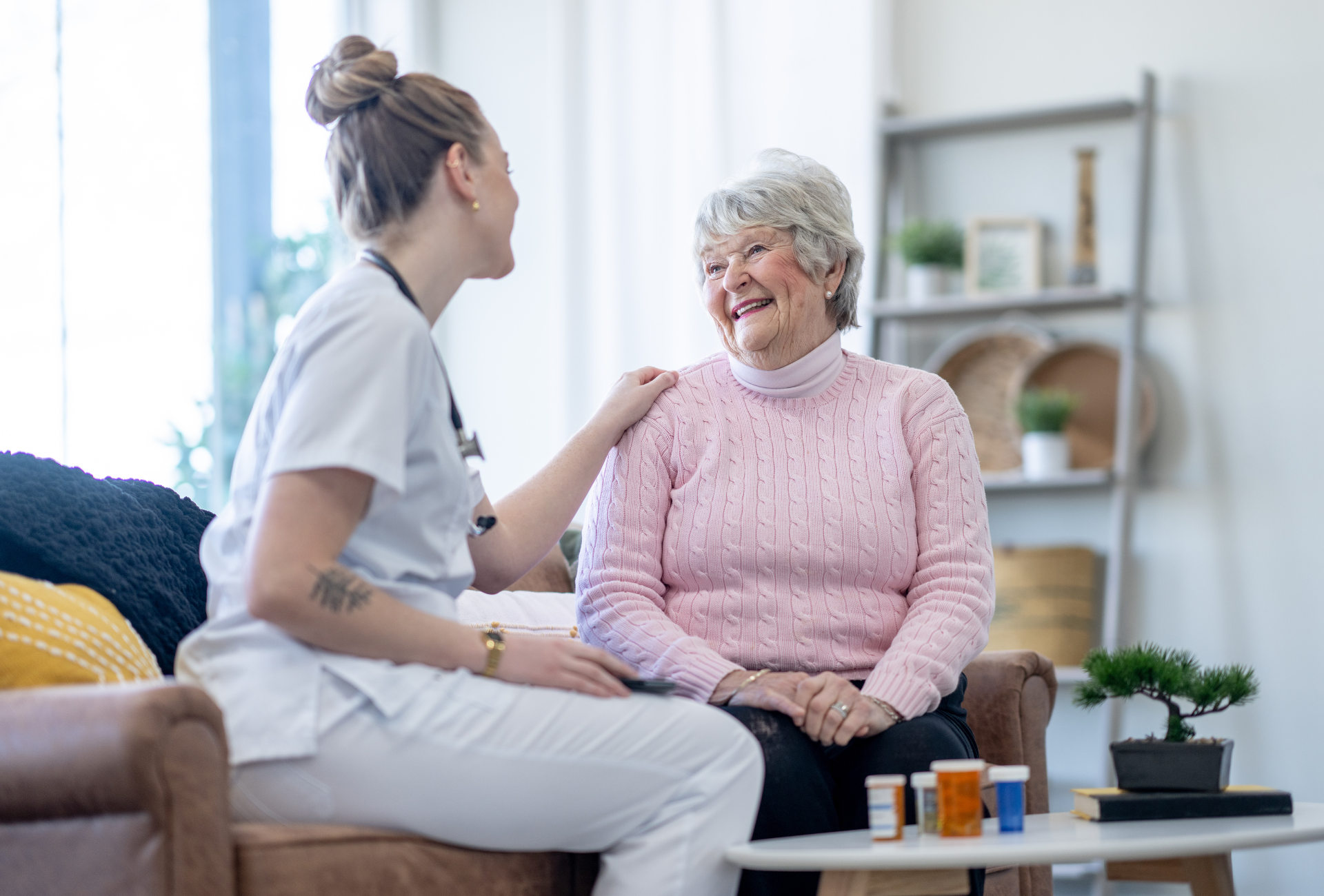 A nurse is talking to an elderly woman who is sitting on a couch.