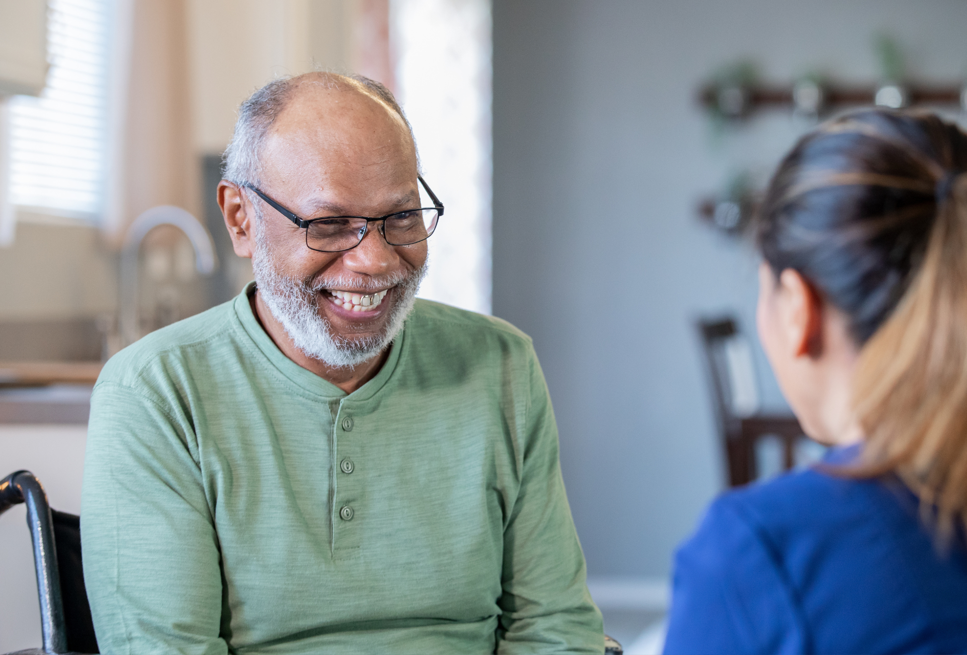 An elderly man in a wheelchair is talking to a nurse.