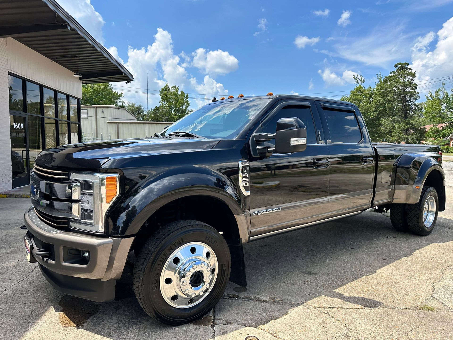 Black Ford F-350 dually pickup truck parked in front of a building on a sunny day.