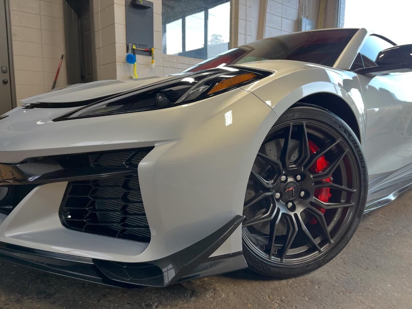 Silver sports car with black rims and red brake calipers parked indoors.