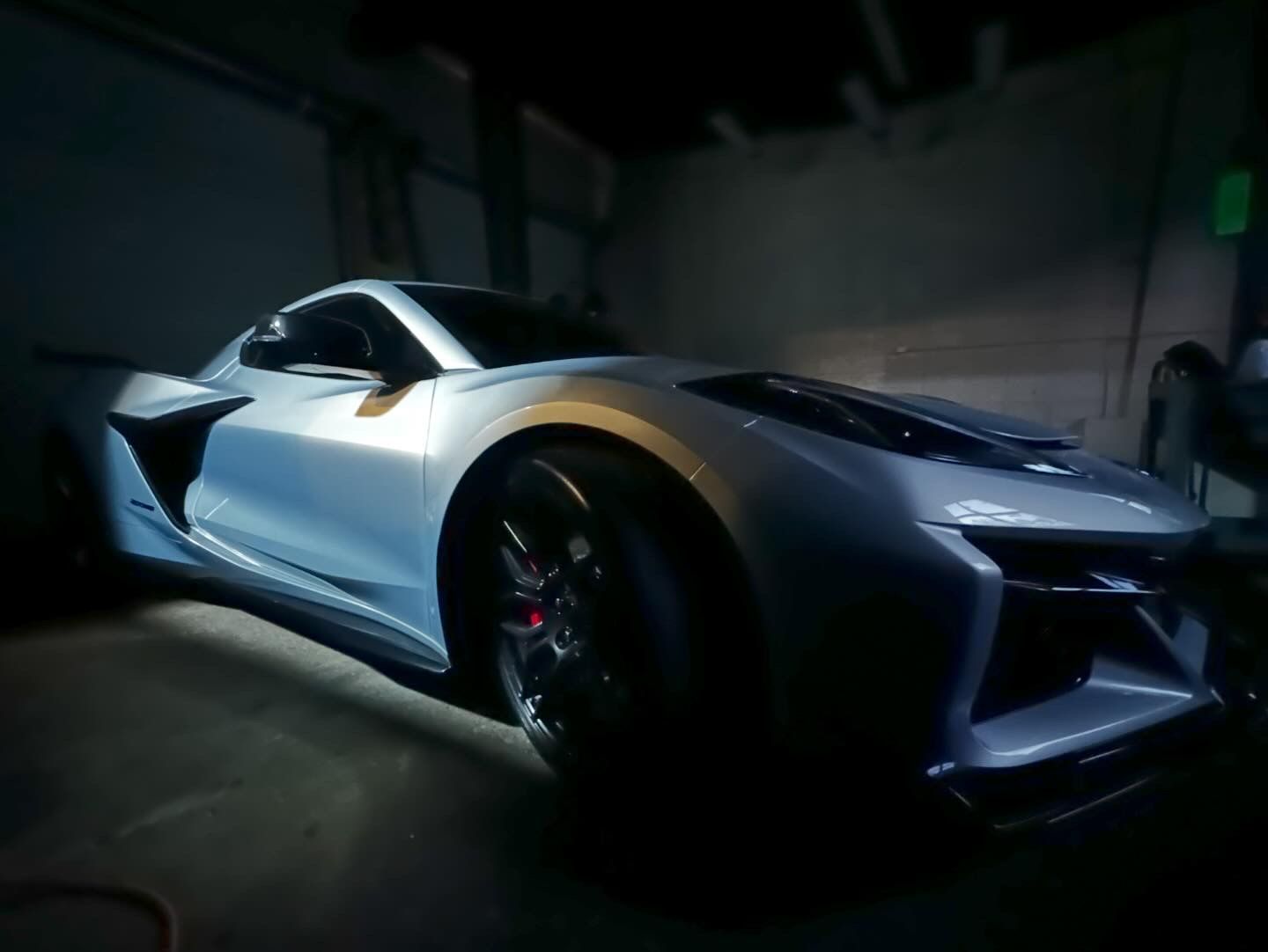 Silver sports car in a dimly lit garage; black wheels, red brake calipers.