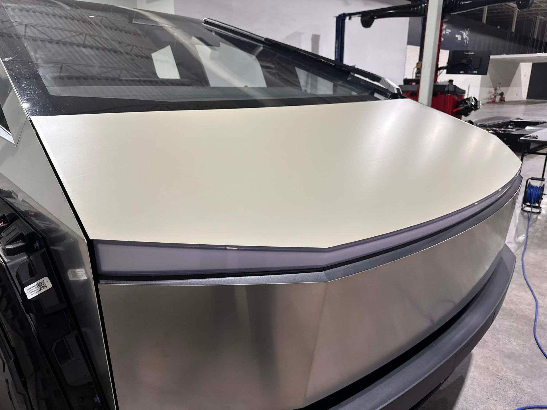 Rear of a Tesla Cybertruck with a matte wrap, showing angular body panels and a dark-tinted rear window in a garage.