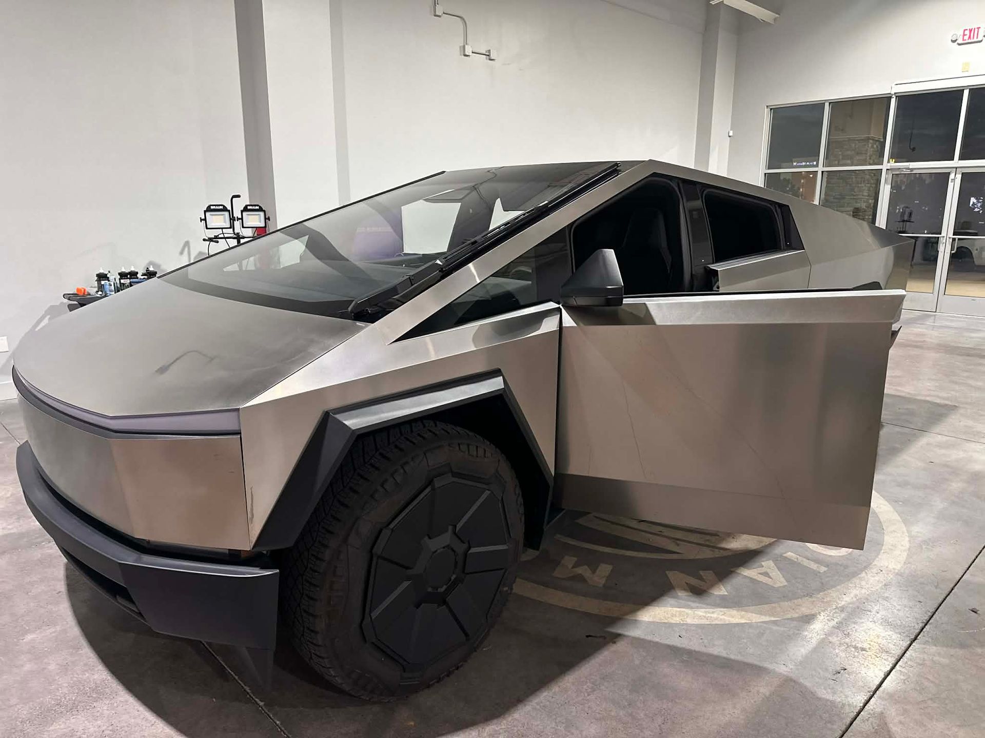 Silver Tesla Cybertruck with door open, parked indoors.
