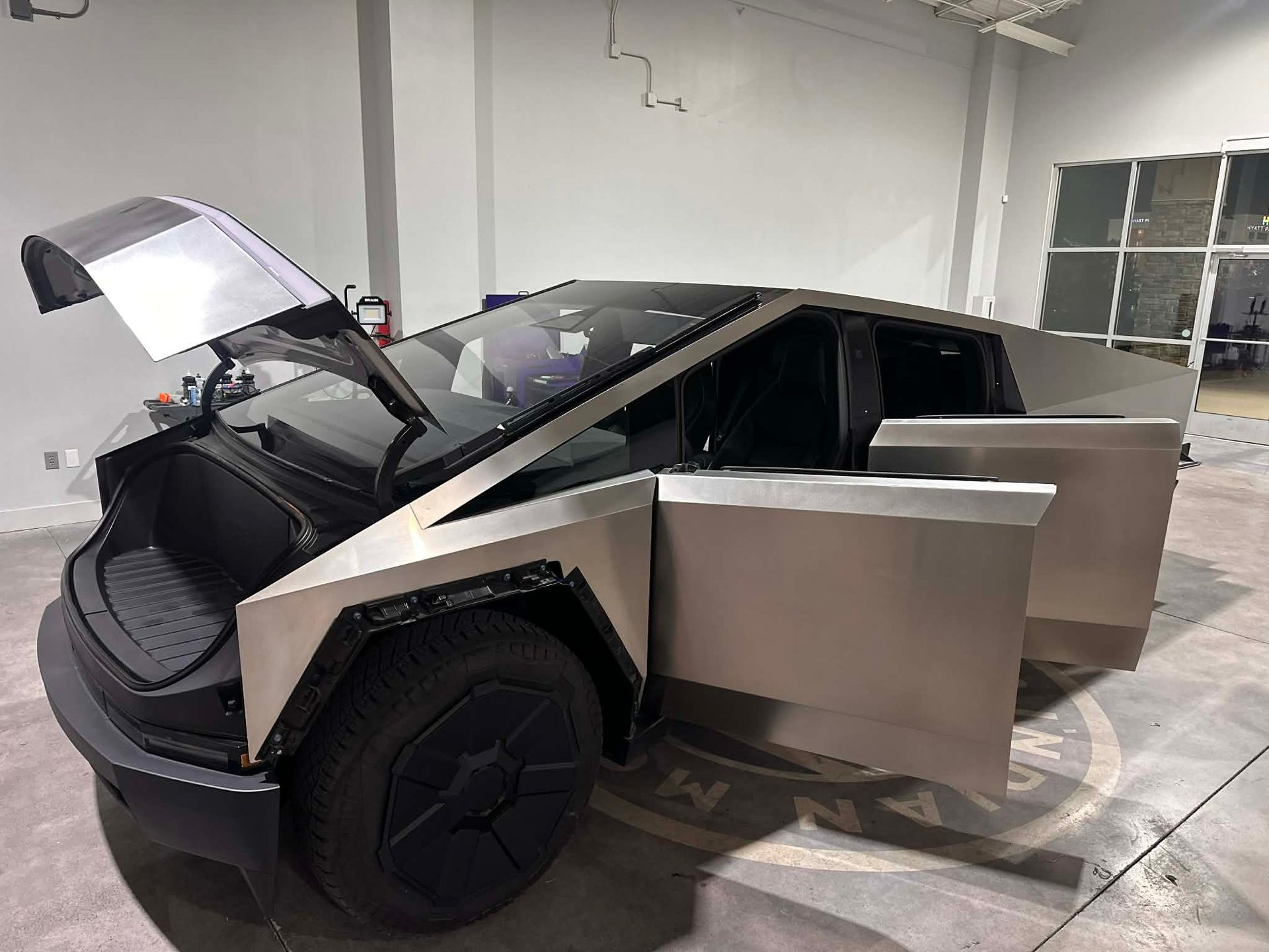 Tesla Cybertruck with doors and hood open in a warehouse.