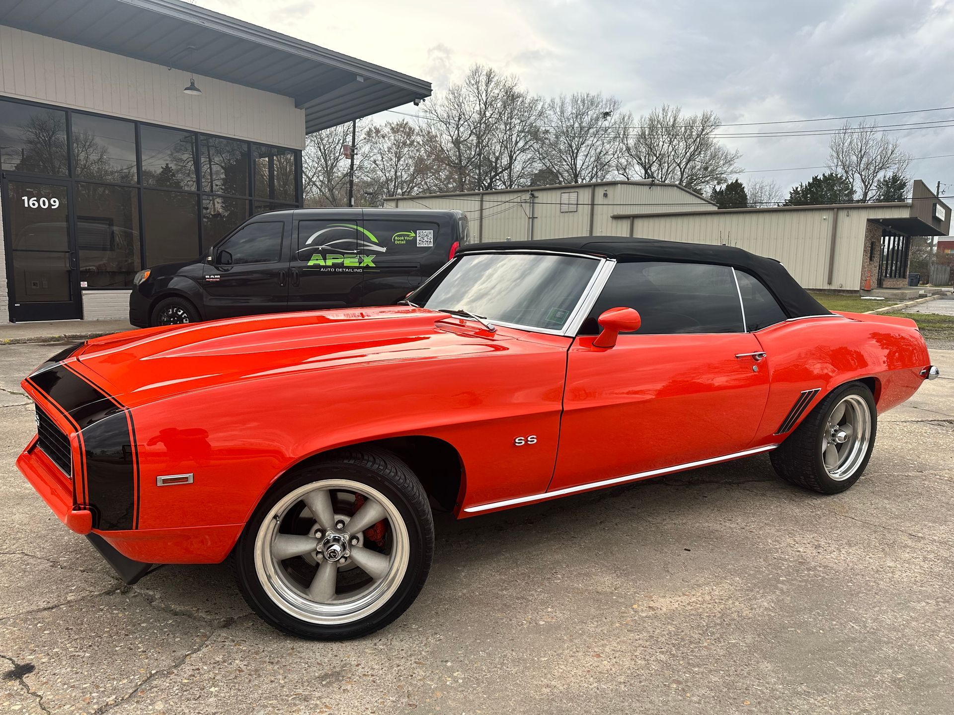 Bright orange classic convertible car parked on concrete, black soft top.