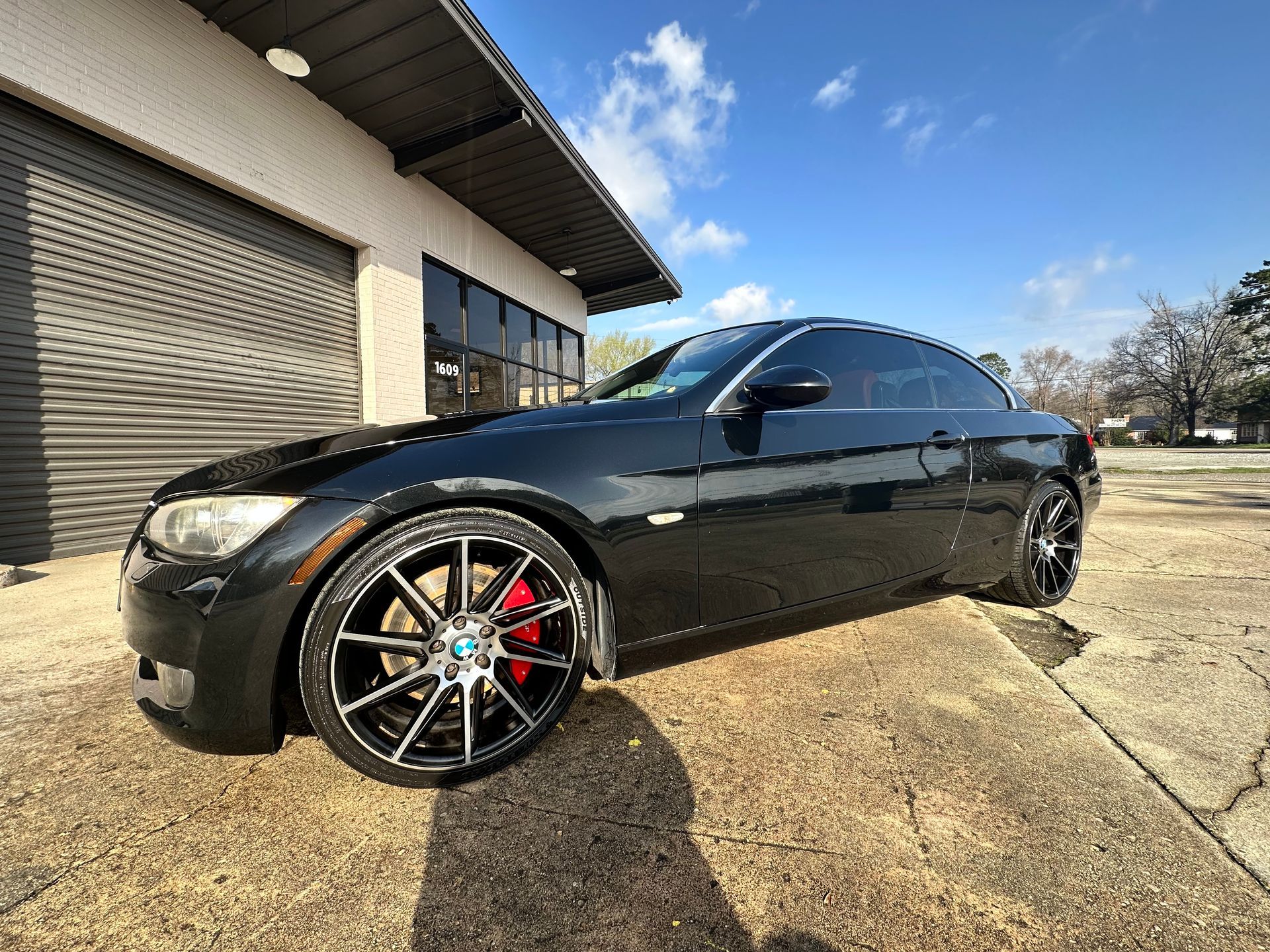 Black BMW coupe with custom wheels parked in front of a building on a sunny day.