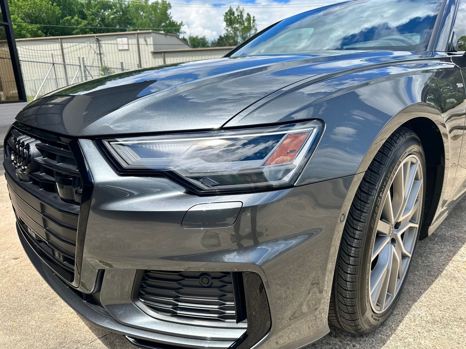Gray Audi sedan, front view, parked outdoors under a partly cloudy sky.