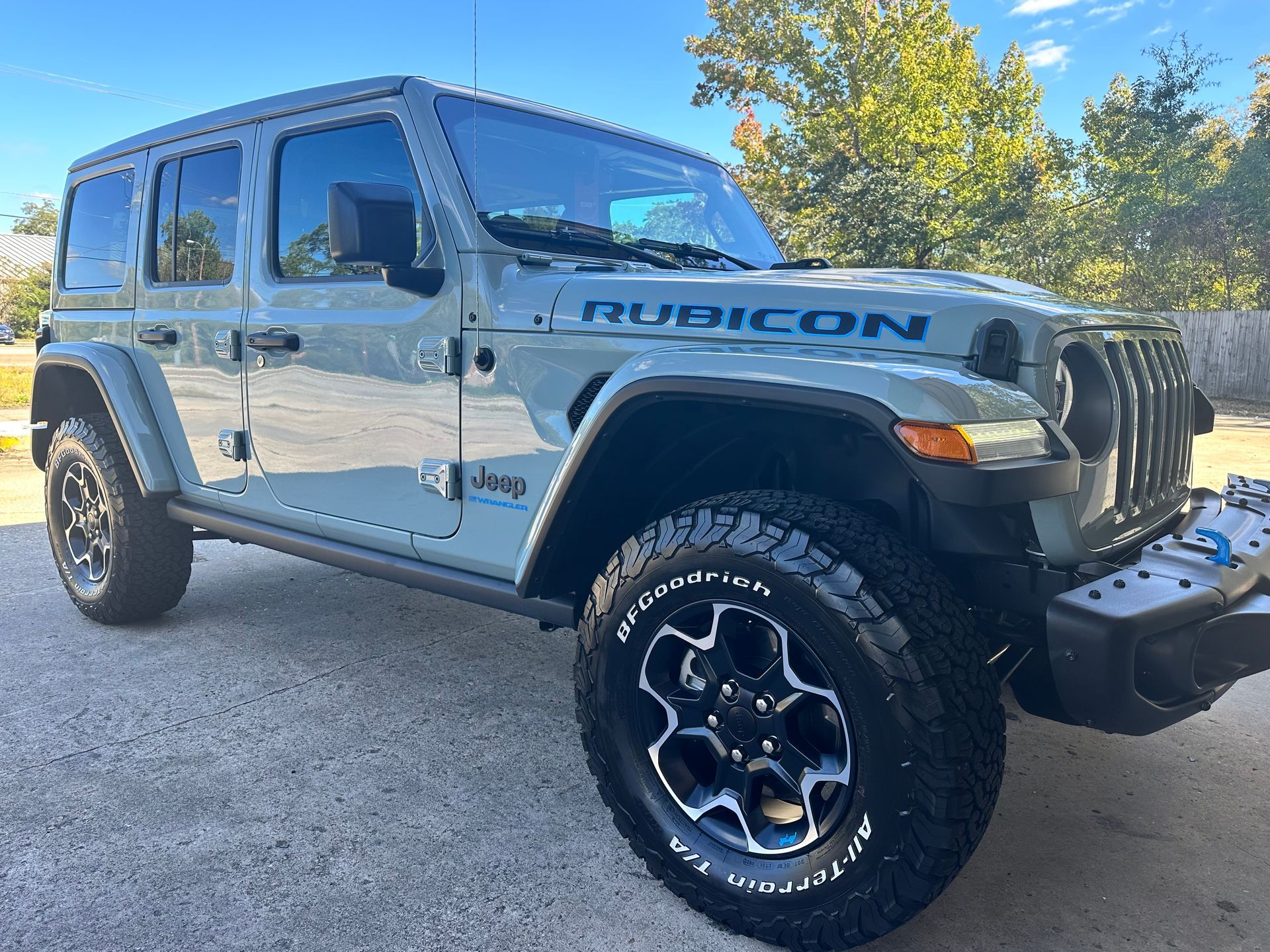 Gray Jeep Rubicon parked outside on pavement.  Black wheels, black grill, and blue lettering.