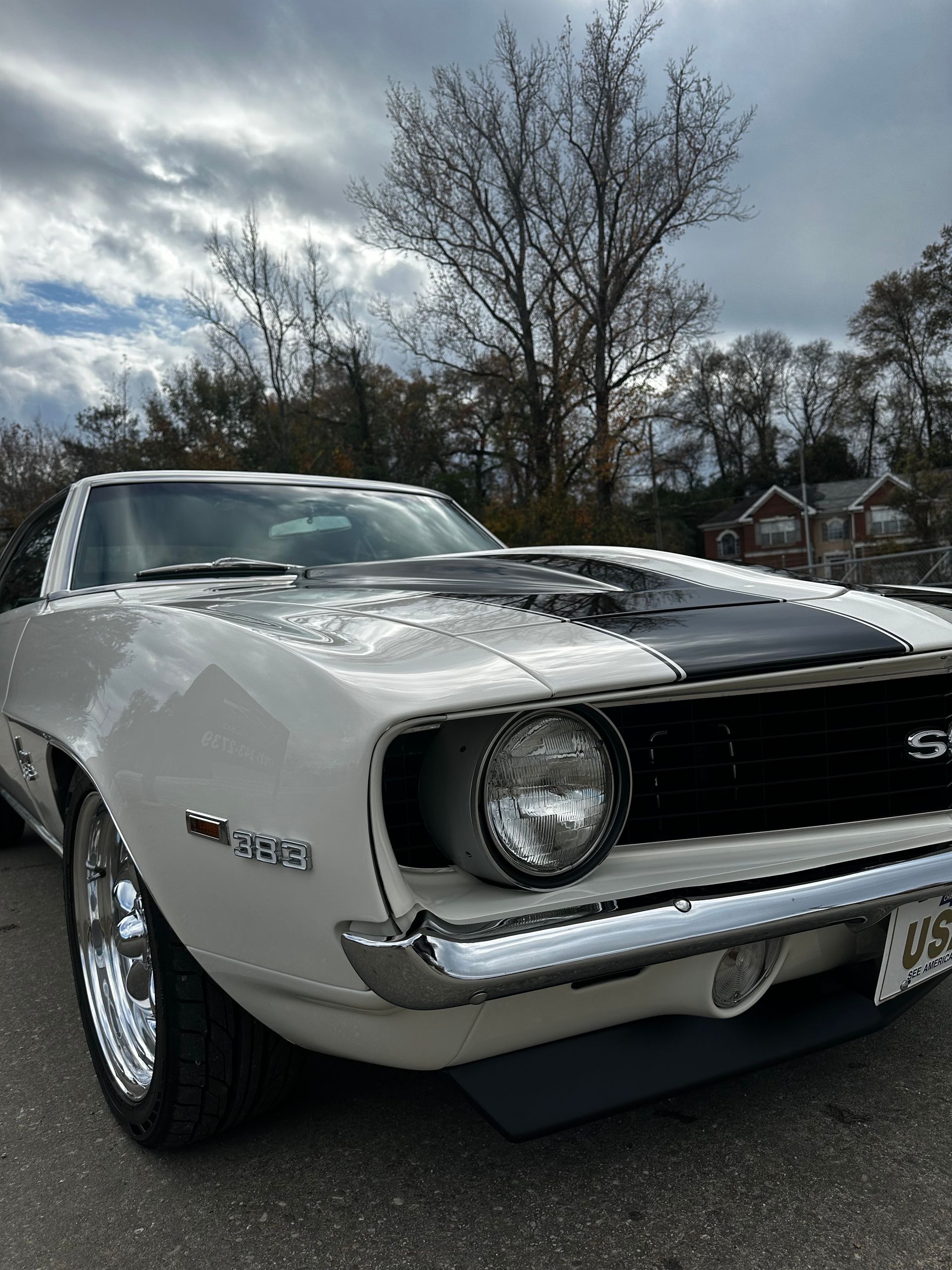 White 1969 Chevrolet Camaro SS with black racing stripes and chrome trim parked outside on a cloudy day.