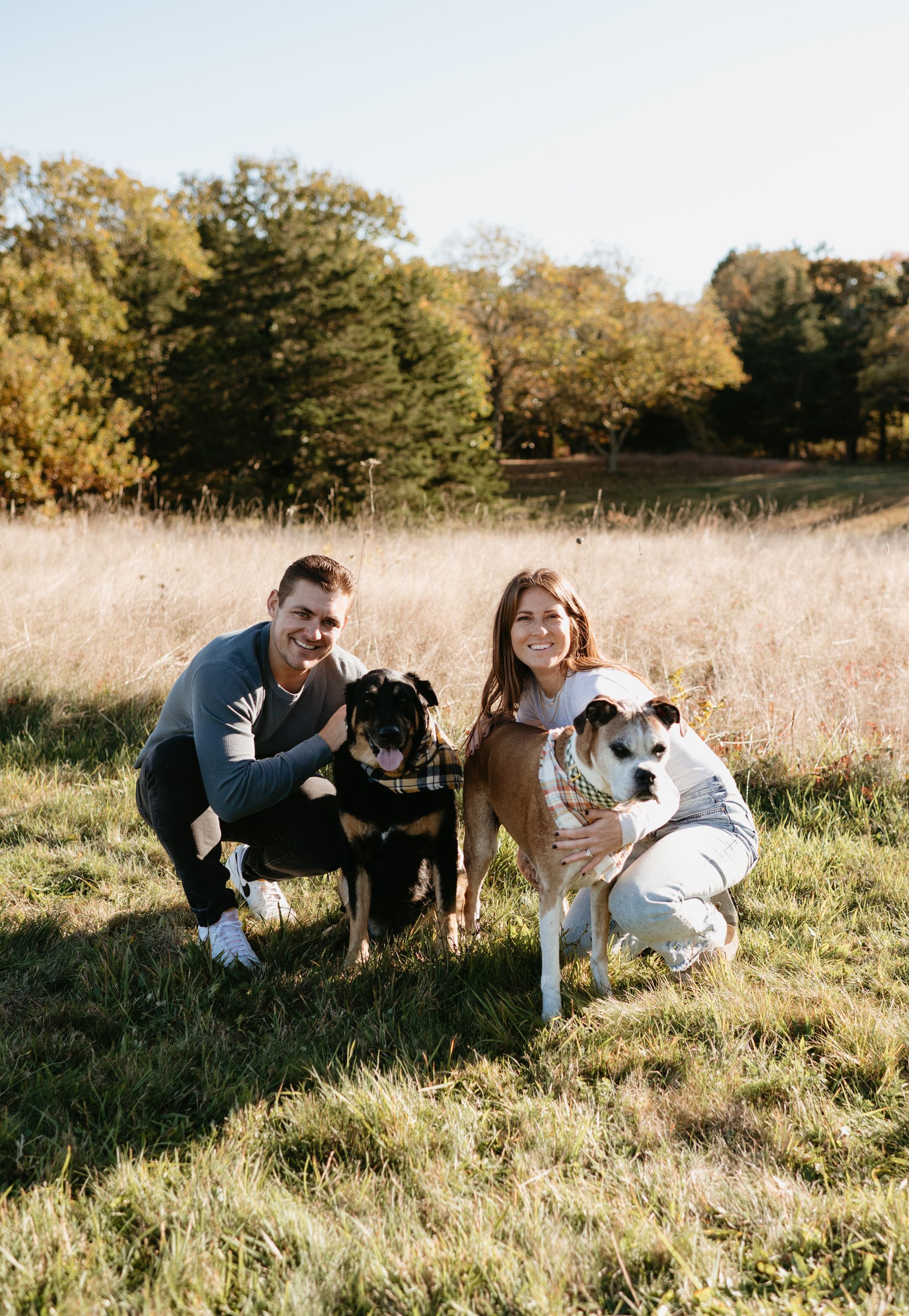 A man and a woman are posing for a picture with their dogs in a field.