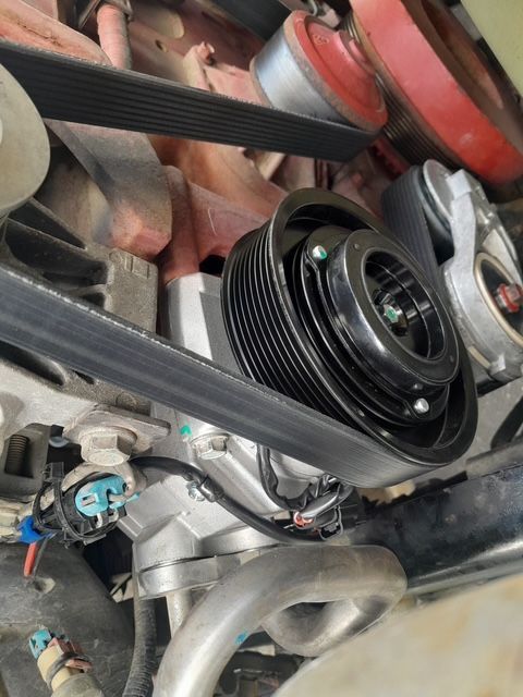 Close-up of a car engine with a black serpentine belt and pulley system in the foreground