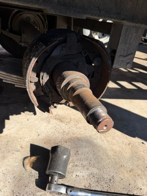Detached car wheel hub and brake assembly exposed under a vehicle, with a removed metal part on the ground.