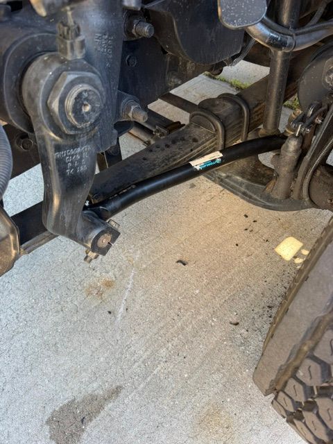 Close-up of a vehicle’s front suspension and axle assembly on a concrete surface.