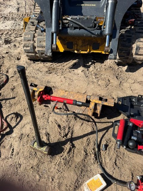 Construction tools on sandy ground near a skid-steer loader bucket