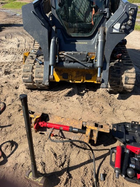 Compact track loader on dirt with hydraulic tools and cables laid out in front of it.