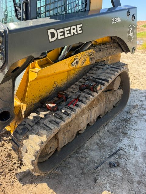 Yellow John Deere compact track loader parked on a muddy worksite, side view with visible rubber tracks