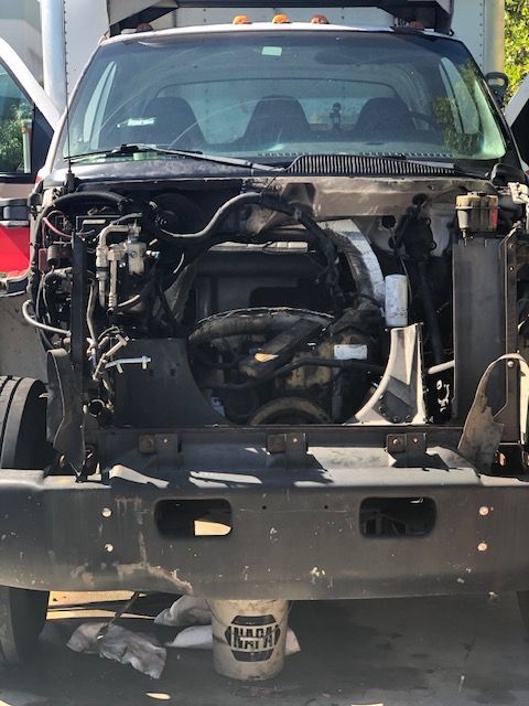 A work truck with the front end disassembled, revealing the engine. The truck is gray.